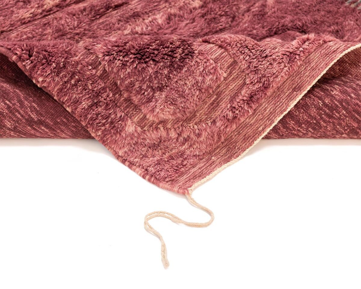 A textured, maroon luxury rug is laid out, showcasing its fluffy surface and looped edging. A loose string is visible, hanging from the edge.