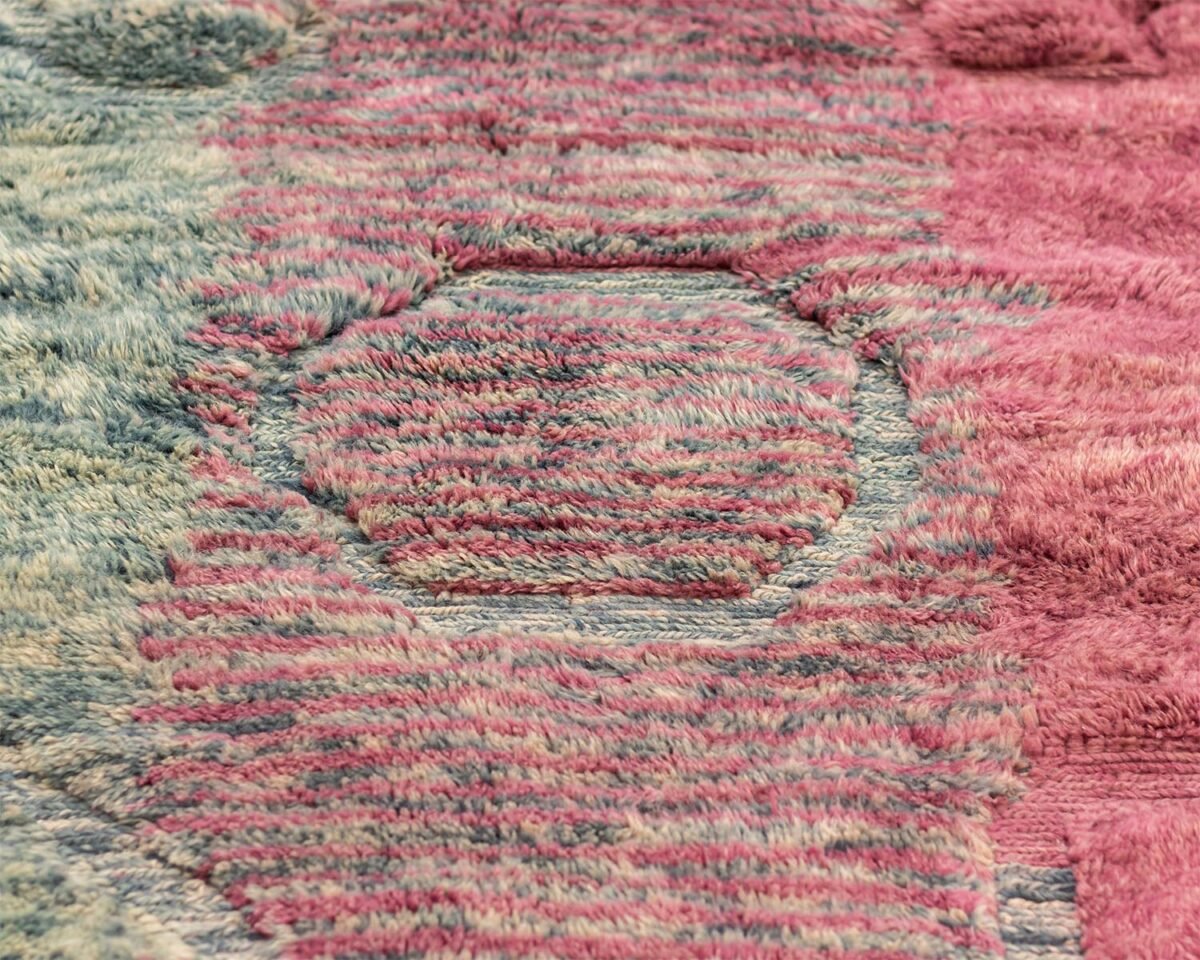 This close-up captures the intricate circular patterns of a luxurious, hand-knotted Moroccan rug. The fabric boasts a stunning blend of textured multicolors, featuring shades of pink, blue, and mauve.