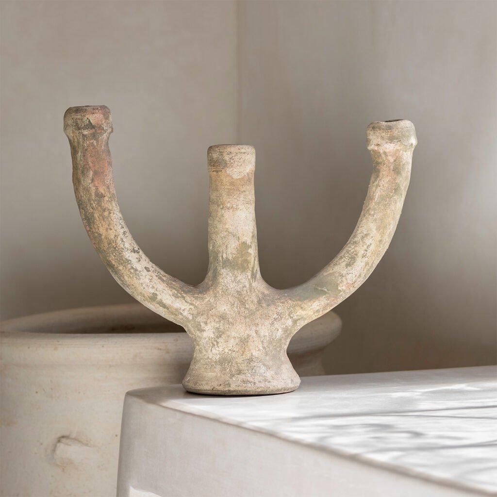 A textured, earthy ceramic sculpture with three prongs stands elegantly on a pristine white base, showcasing its natural beauty.