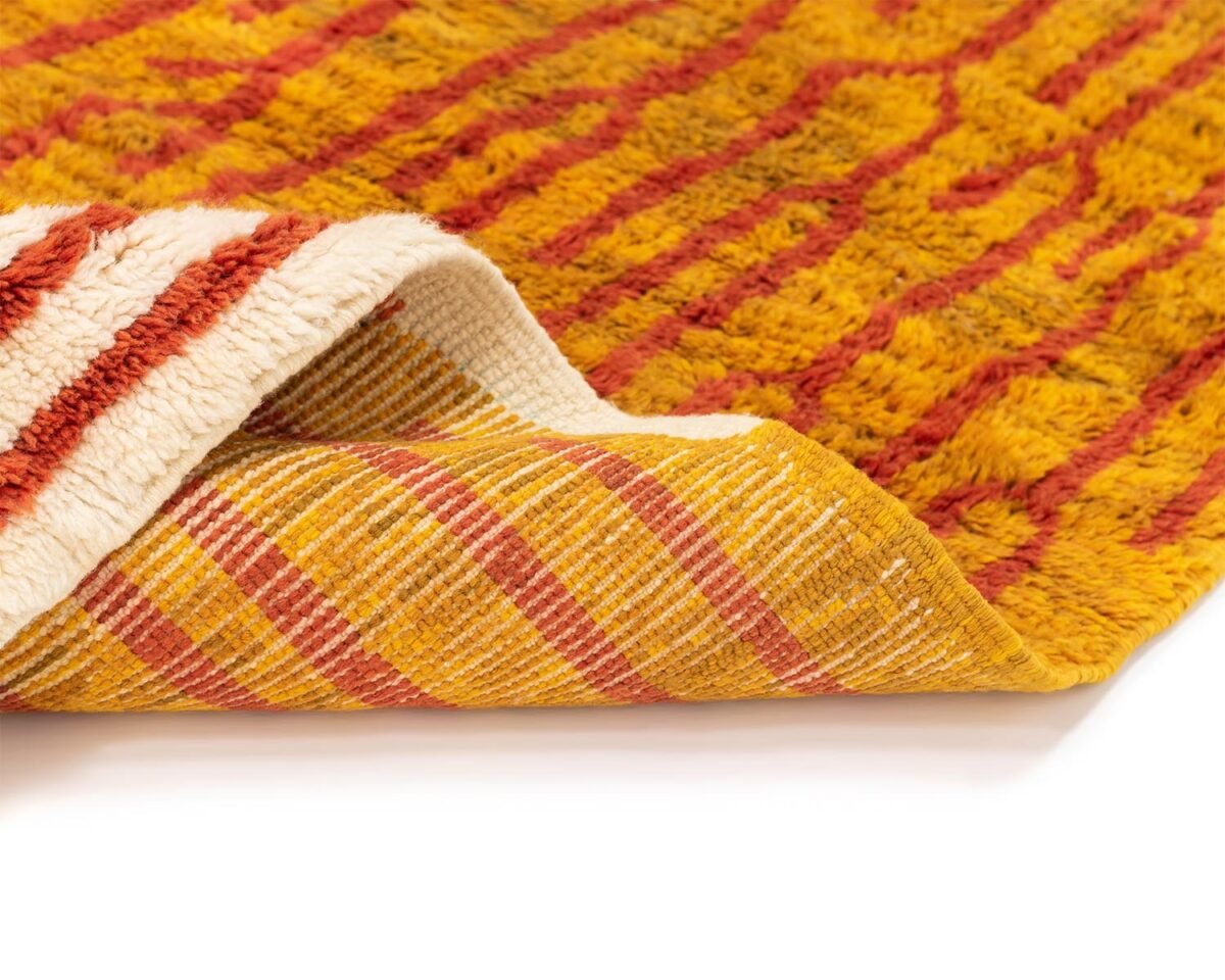 This close-up showcases a corner of a hand-knotted, textured reversible rug with luxurious orange and red patterns. One side features fluffy lines, while the other side displays a flat, plaid design—a true masterpiece of handmade home decor.
