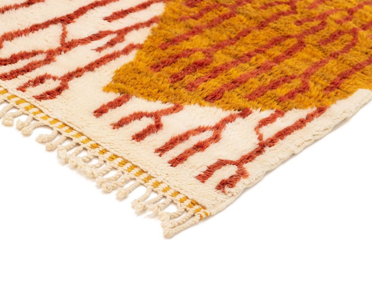 Close-up of a luxury rug corner with a warm abstract pattern in red and gold on a cream background, featuring fringe on the edges, perfect for adding handmade home decor elegance.