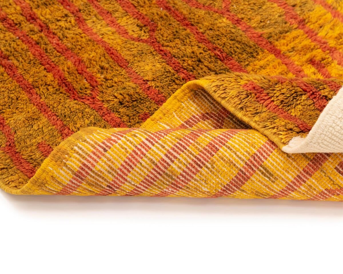 This luxury rug features a folded design with vibrant orange and yellow textures and a plaid pattern on the reverse side. Expertly hand-knotted, this exquisite piece reflects the finest in handmade home decor.