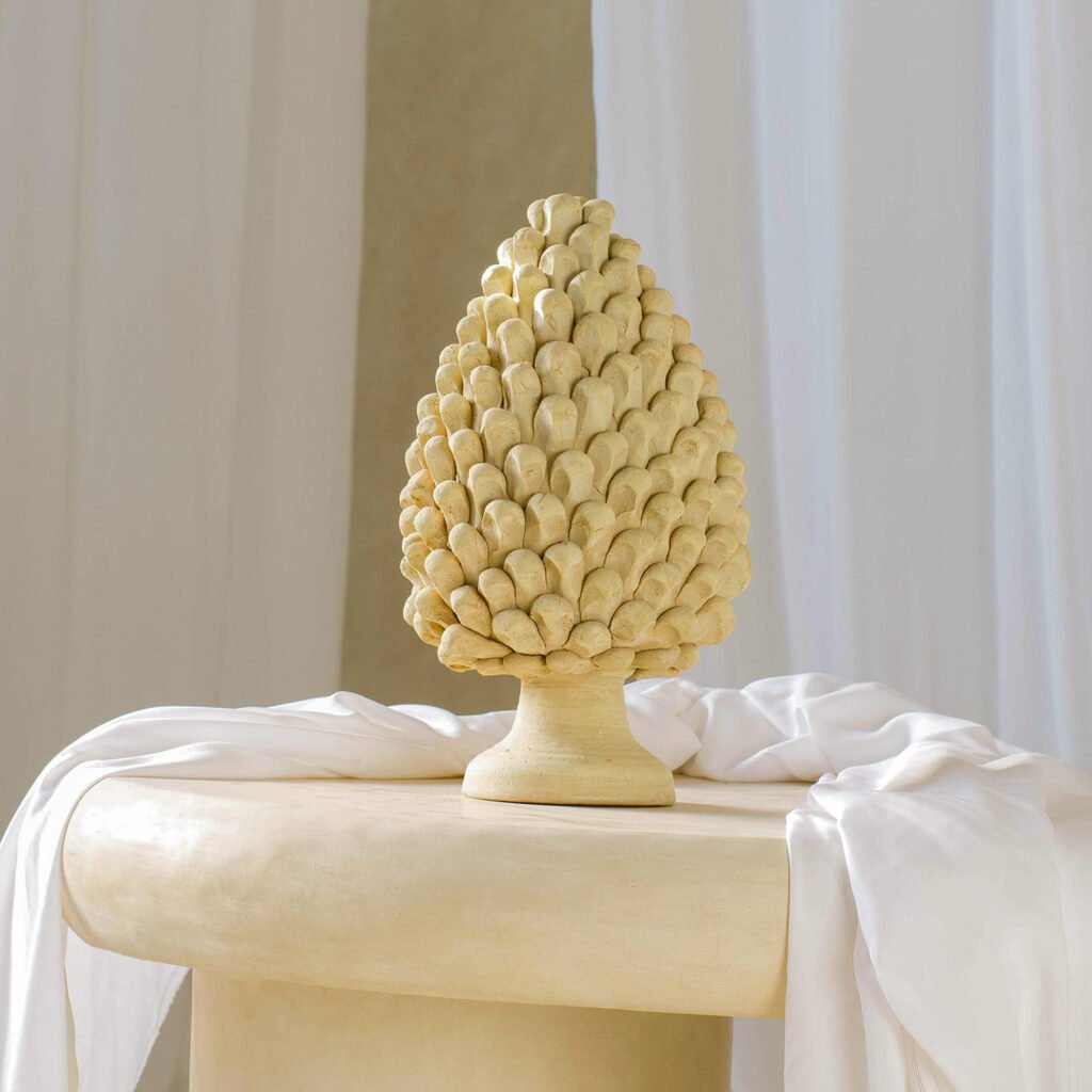 A vibrant yellow ceramic pine cone sculpture sits elegantly on a pedestal covered in soft white fabric, framed by a backdrop of pristine white curtains, creating a striking visual centerpiece.