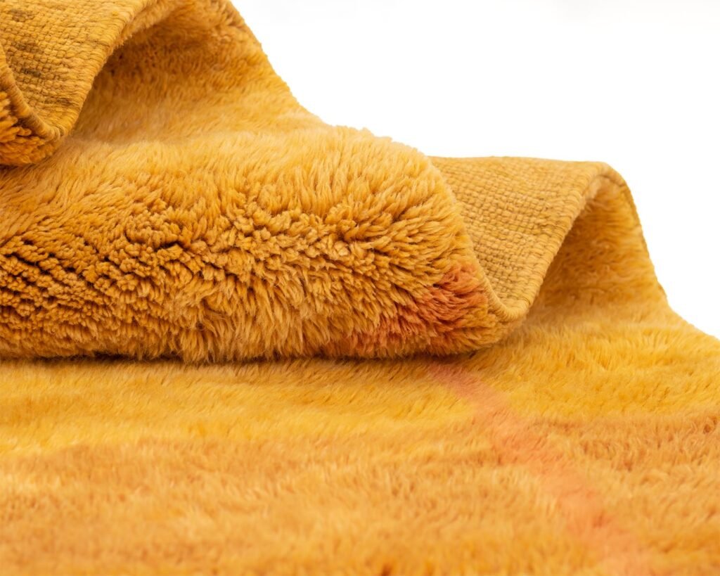 Close-up of an orange, fluffy, fleece that reveals a hand-knotted rug-like texture with delicate folds and layered details.