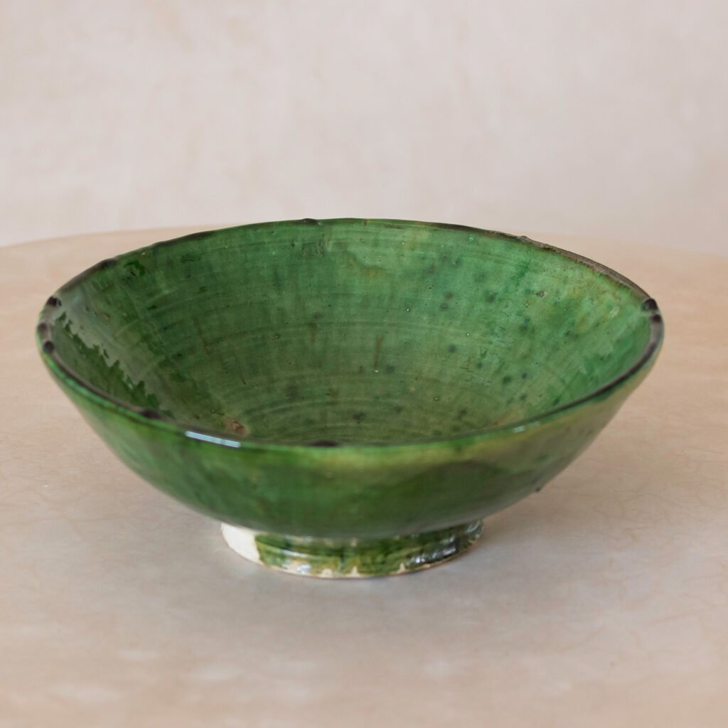 A vibrant green ceramic bowl with a shiny glaze rests elegantly on a beige surface, adding a touch of natures essence to any space.
