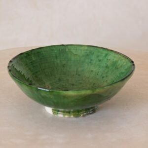 A vibrant green ceramic bowl with a shiny glaze rests elegantly on a beige surface, adding a touch of natures essence to any space.