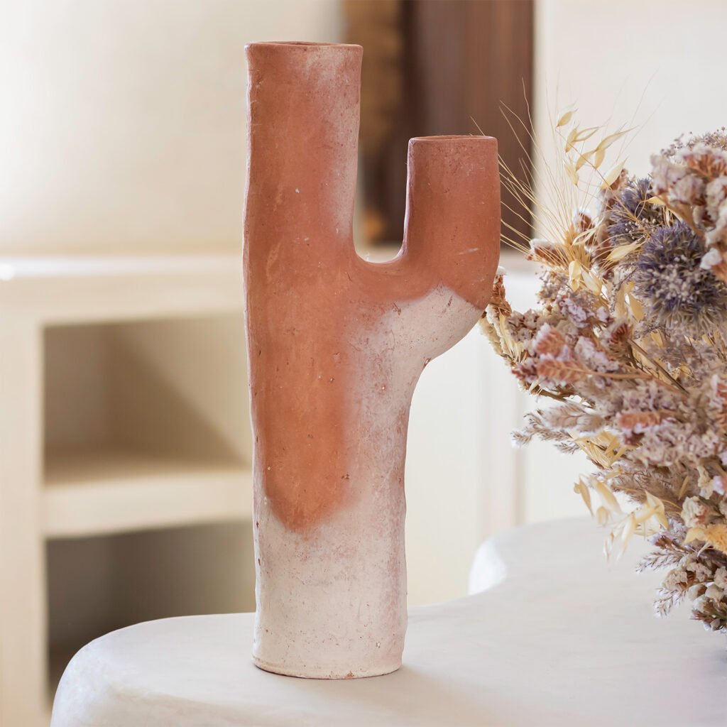 A two-toned ceramic vase shaped like a cactus stands on a white surface, accompanied by a delightful arrangement of dried flowers.