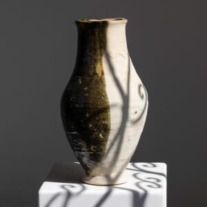 A two-toned ceramic vase sits elegantly on a white pedestal, casting intricate shadow patterns that captivate the eye.