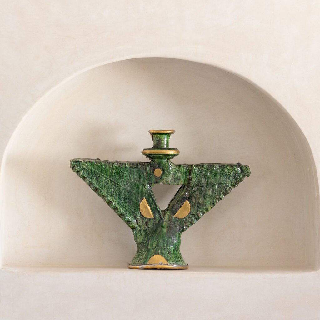 A green, tree-shaped ceramic sculpture with gold accents and a central circular cutout is elegantly showcased on a pristine white recessed shelf, exuding an aura of natural grace.
