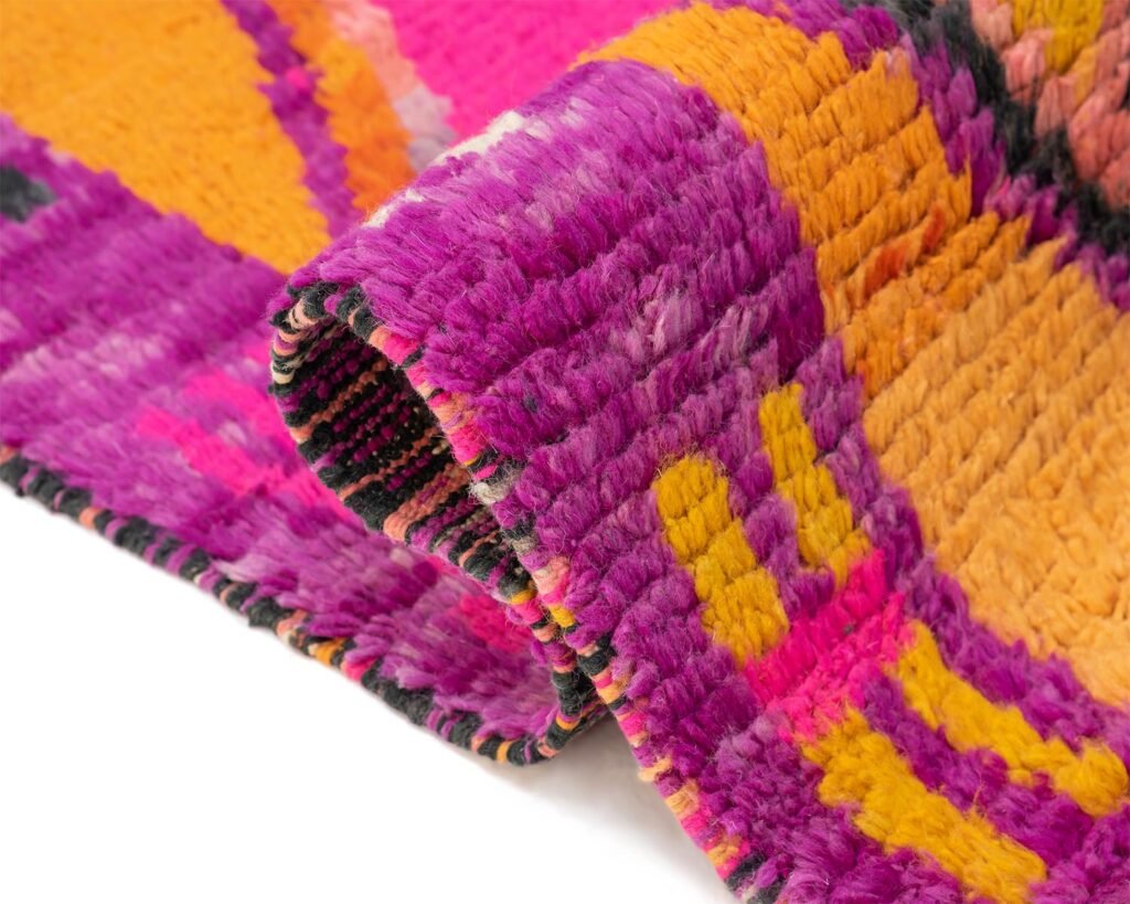 A close-up of a vibrant, multicolored textile showcases pink, orange, and yellow patterns with a thick, woven texture.