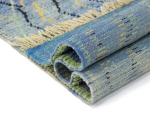 A folded blue woven rug with beige fringe and intricate black-and-yellow details elegantly graces a white surface, adding a touch of style to the room.
