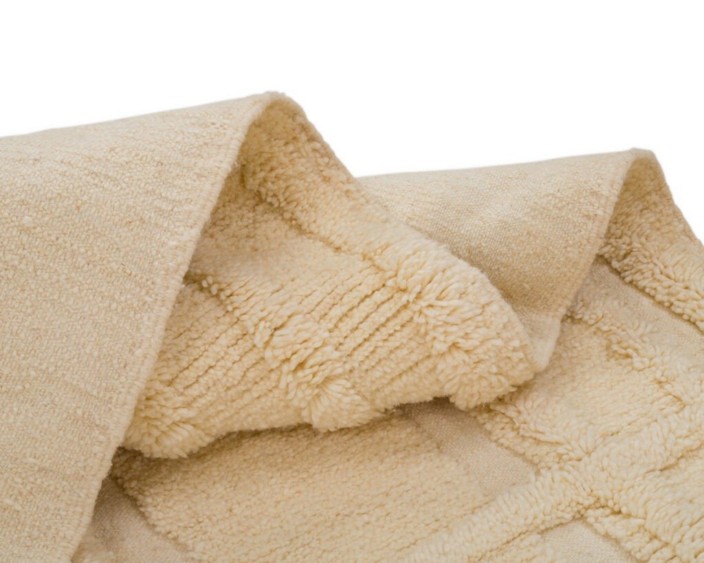 A soft, beige textured accessory folded with one corner turned over, revealing a hand-knotted interior akin to a fine runner rug.