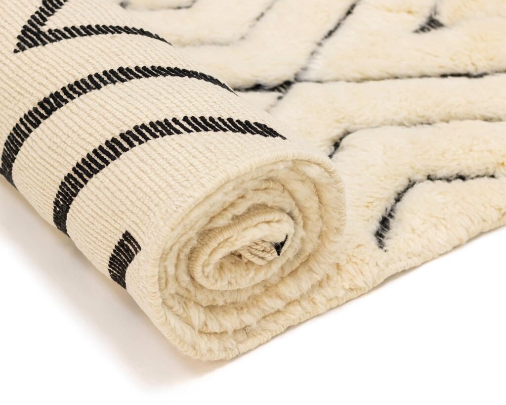 A rolled-up beige rug with black geometric patterns seamlessly combines style and functionality, making it an ideal addition to any modern space. Set against a white background, its intricate design adds a touch of elegance to your decor.