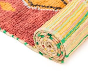 A rolled-up runner rug showcases a vibrant red, yellow, and black pattern on its visible surface, complemented by a multicolored striped underside.
