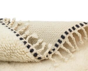 A close-up of a folded cream-colored woven runner rug with black fringe detailing and tassels.