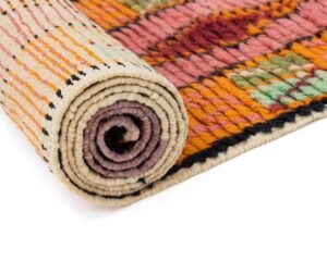 This vibrant runner rug features a rolled-up design with geometric patterns in orange, pink, green, and cream.