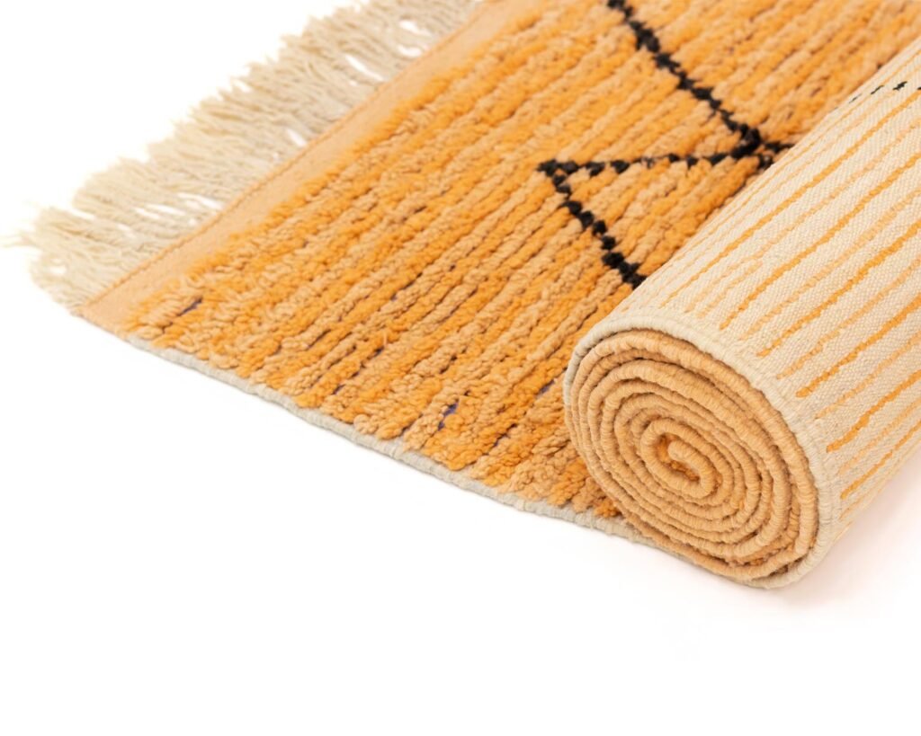 A vibrant rolled orange runner rug with black geometric patterns and fringe on the edge is elegantly positioned on a pristine white surface.