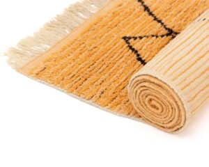 A vibrant rolled orange runner rug with black geometric patterns and fringe on the edge is elegantly positioned on a pristine white surface.