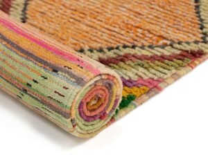 A vibrant woven rug features a striking blend of pink, green, orange, and black patterns set against a crisp white background.