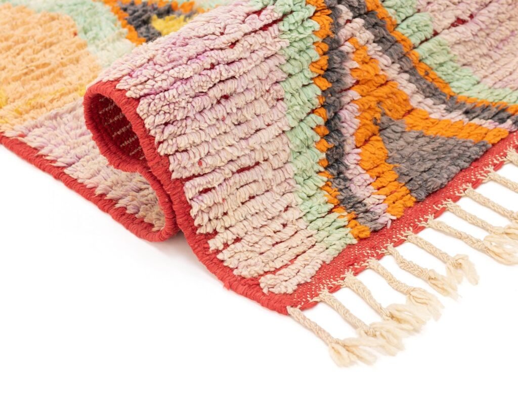 A vibrant, folded runner rug with an abstract pattern and fringed edge rests on a white surface.