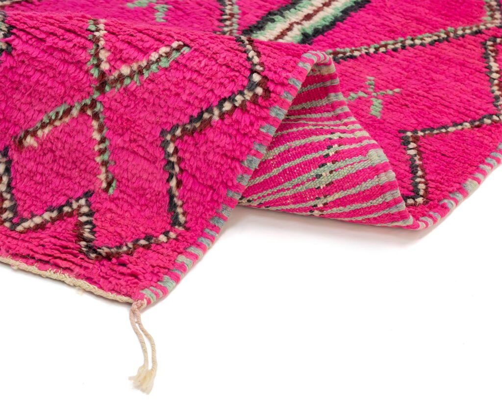 This vibrant pink textile showcases a geometric pattern in dark and light tones. The edges are slightly folded, revealing an underside with green and pink stripes accompanied by a loose string. Ideal for adding a pop of color and style to any space.