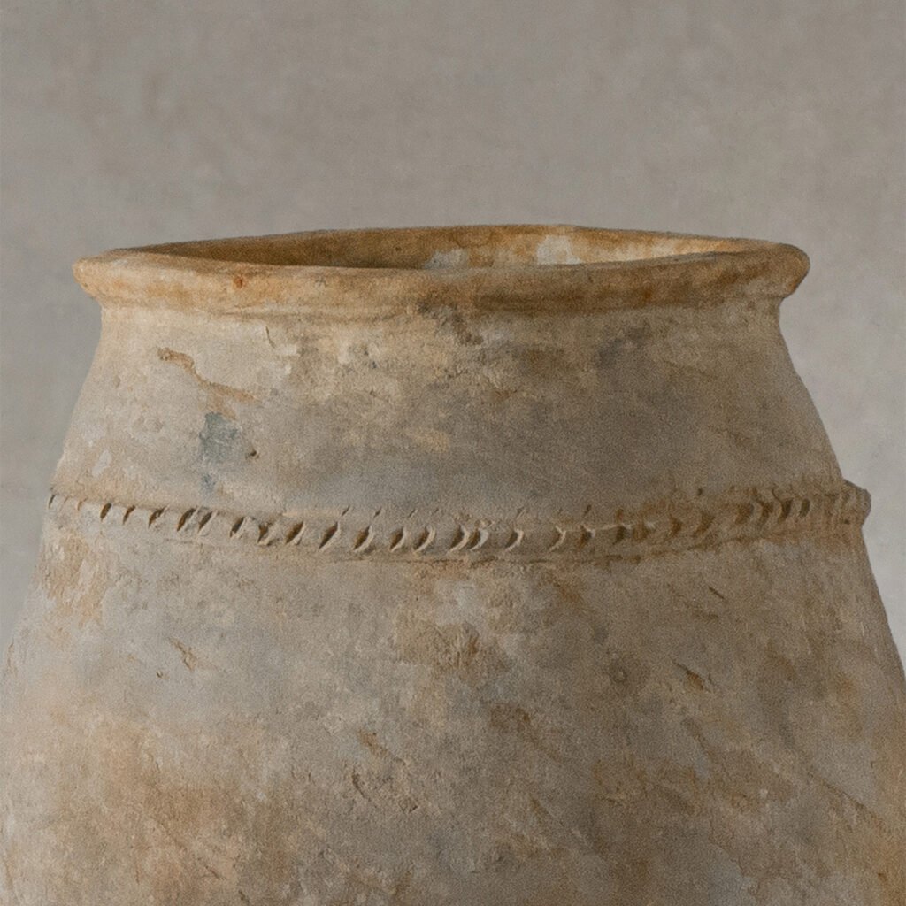 Close-up of the top portion of an ancient, weathered clay pot with a textured surface and a decorative horizontal band, echoing the craftsmanship found in vintage Berber jars.