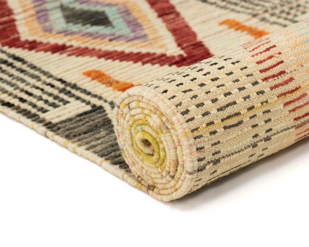 A vibrant, rolled-up carpet showcases geometric patterns in shades of beige, red, orange, and gray. The intricate design adds a touch of elegance to any room decor.