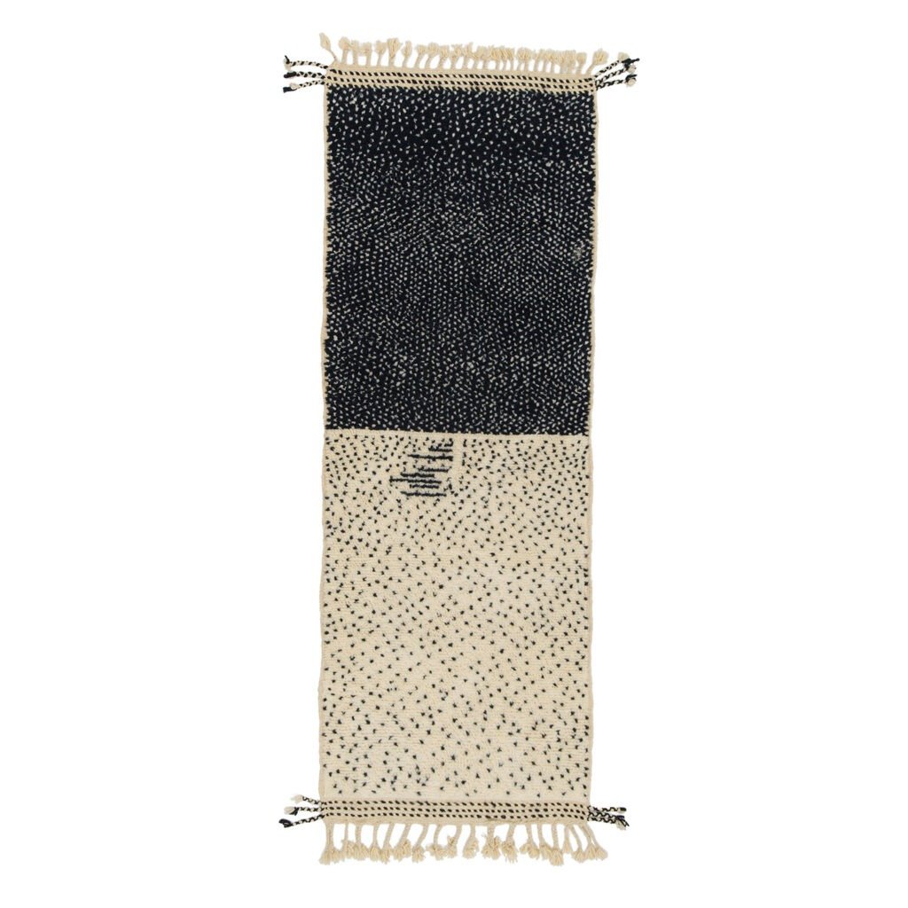 This rectangular runner rug boasts a speckled pattern with a charming fringe. The top half is dark adorned with white specks, while the bottom half is light featuring dark specks, creating a perfect blend of contrast for any space.