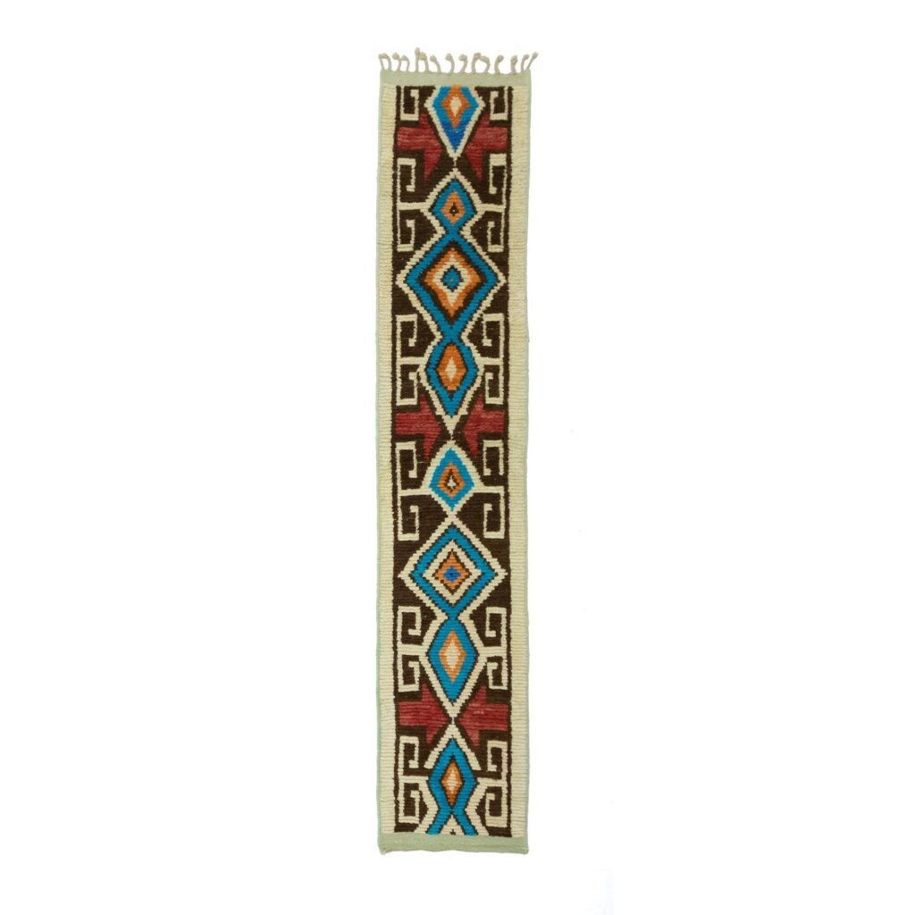 A long, narrow woven rug with tribal geometric patterns in blue, red, brown, and beige features diamond and rectangular shapes along with small fringe details at the top.