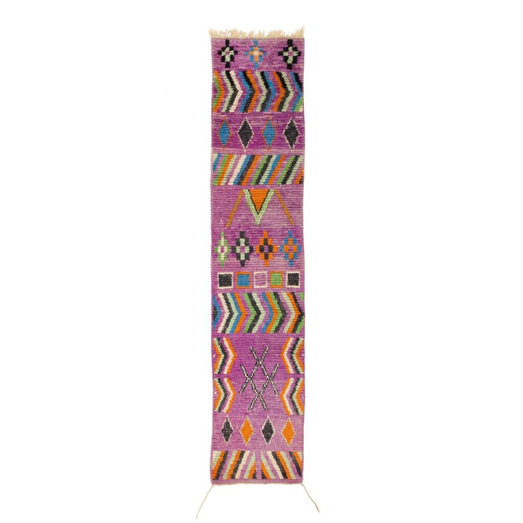 A colorful, narrow runner rug features geometric patterns on a predominantly purple background.