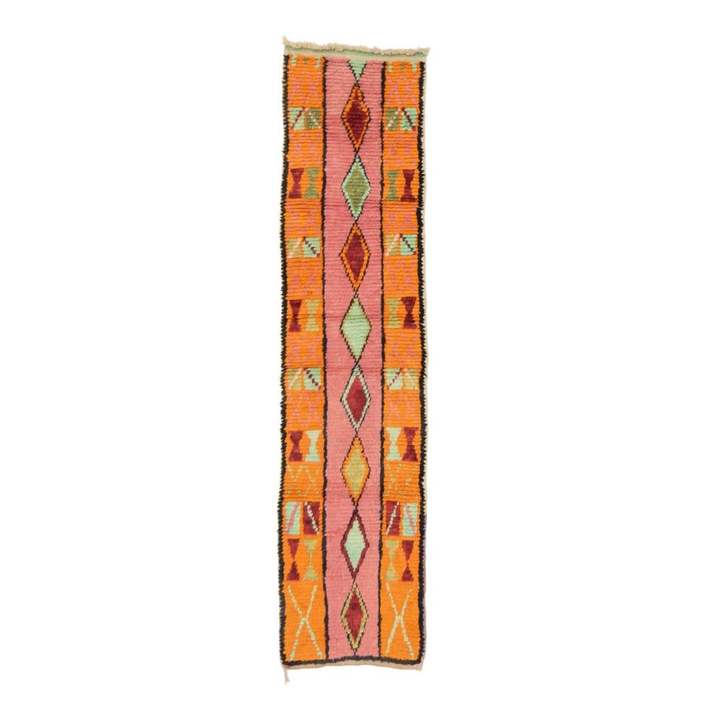 A vibrant runner rug featuring orange, pink, green, and red diamond and triangle shapes set against a crisp white background.