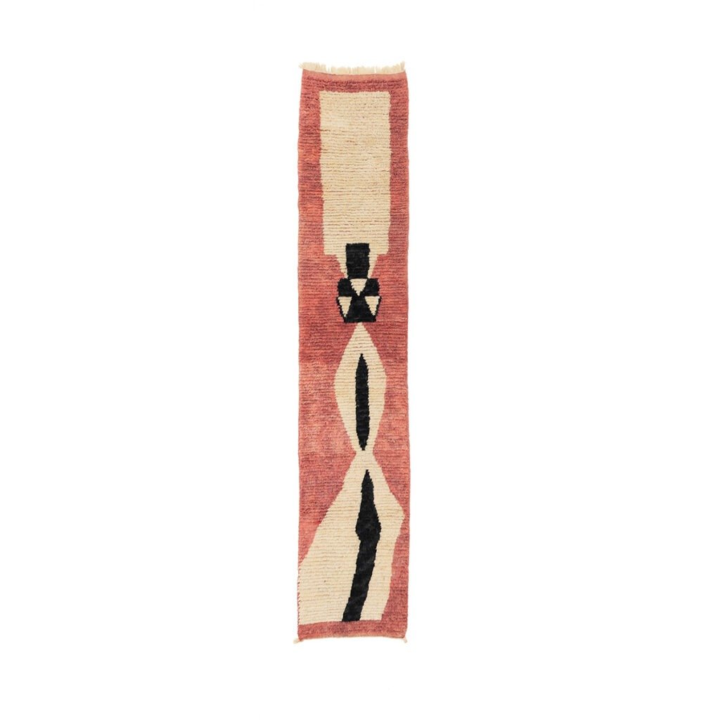 A runner rug with a narrow, vertical design features geometric patterns in black, beige, and reddish-brown on a white background.
