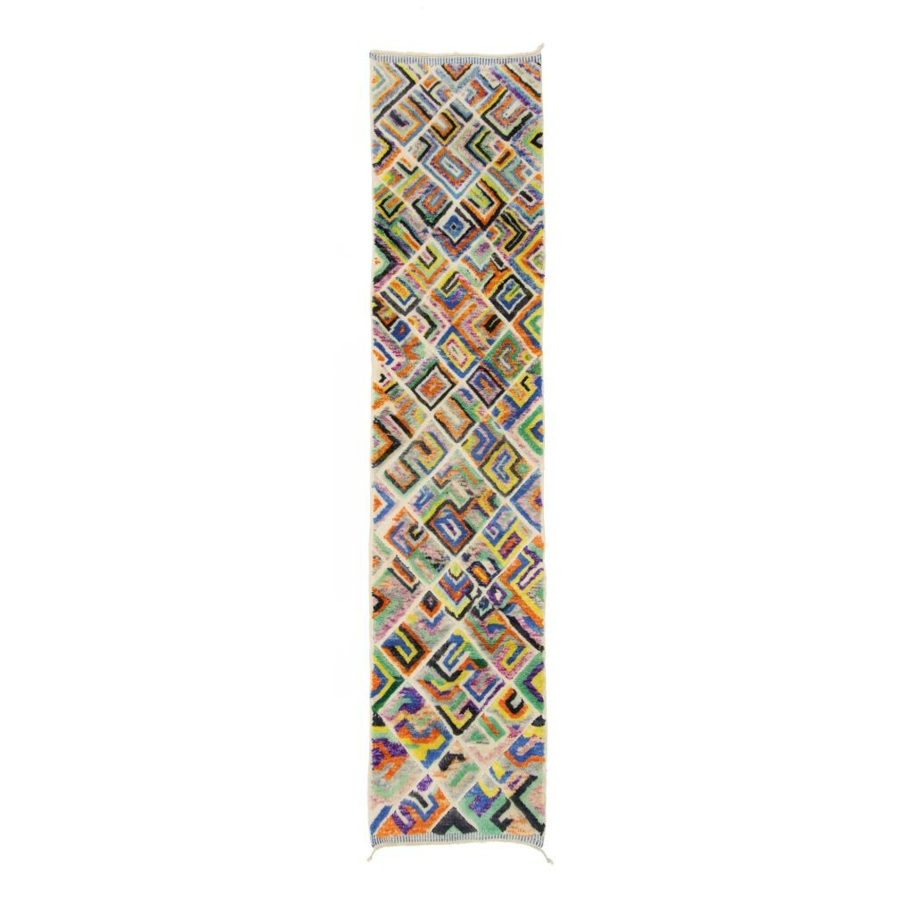 A long, narrow runner rug with a colorful geometric pattern featuring interconnected shapes and lines on a white background.