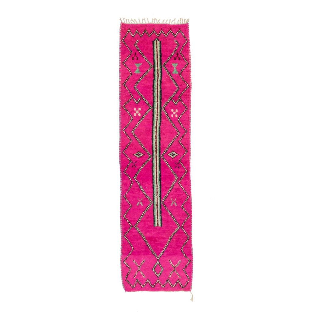 A vibrant pink rug with a geometric pattern in black and green, featuring diamond shapes and zigzags, showcased on a white background, adds a stylish flair to any space.