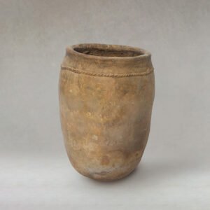 A large, aged clay pot with a narrow opening and a rounded base stands prominently. Decorative lines gracefully encircle the top. The pot boasts a rough texture and weathered appearance, set against a minimalistic backdrop.