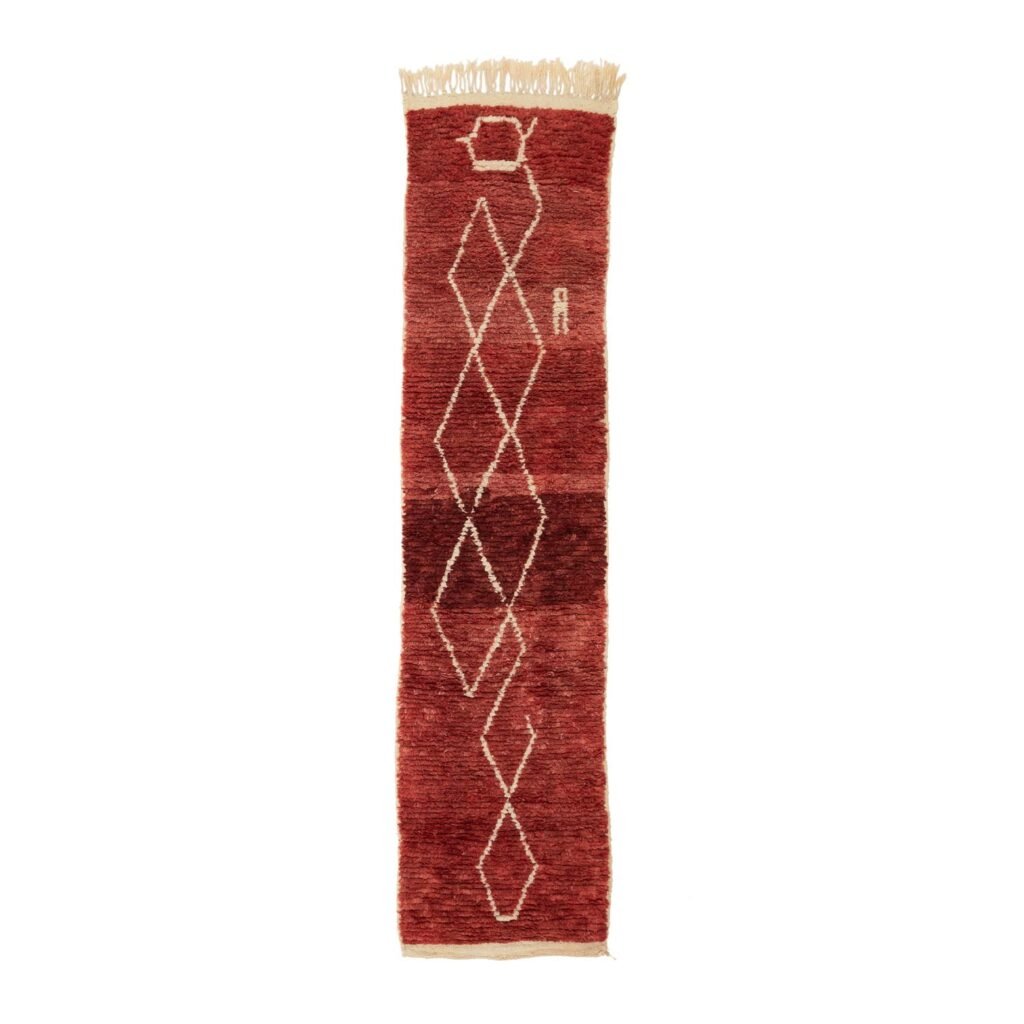 A narrow, red runner rug with a fringe on both ends showcases a central geometric pattern of intricate interlocking white diamonds, adding an elegant touch to any hallway or living space.