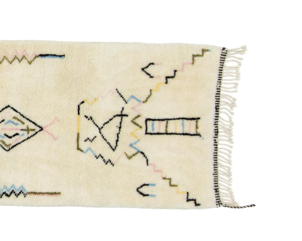 A cream-colored rug featuring abstract geometric patterns in vibrant hues, complete with fringes on one side, adds a bold touch to any room.