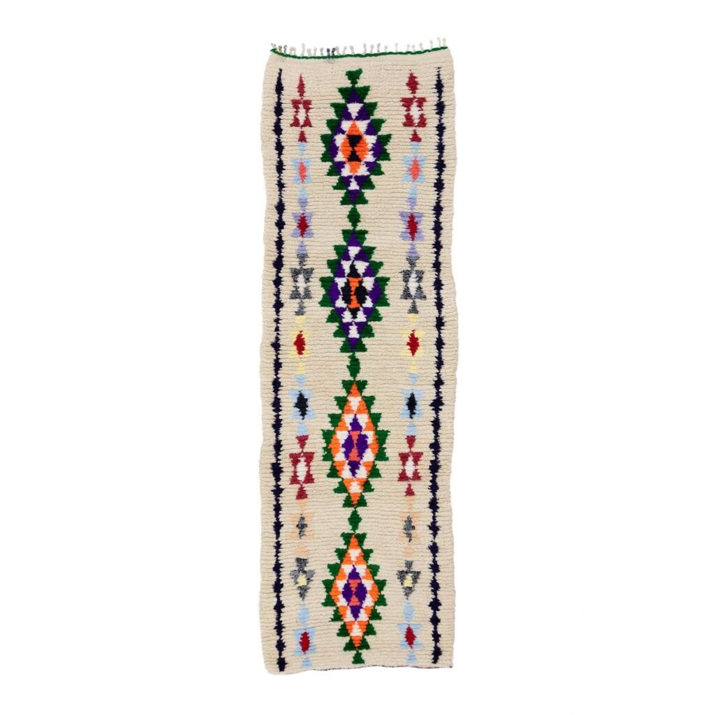 A long, narrow woven rug featuring vibrant geometric patterns like diamonds and triangles set against a light background adds a touch of elegance to any room.