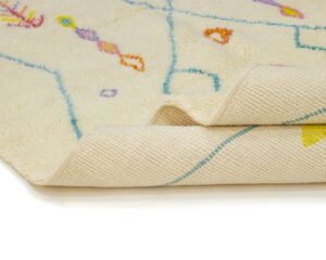 Close-up of a hand-knotted beige rug with a colorful pattern, showcasing its edge and underside texture on a pristine white background.