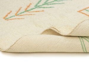Close-up of the corner of an artisanal rug, showcasing the beige fabric adorned with abstract green and orange patterns. The texture of the hand-knotted design is visible, offering a glimpse of its authentic craftsmanship from Morocco.