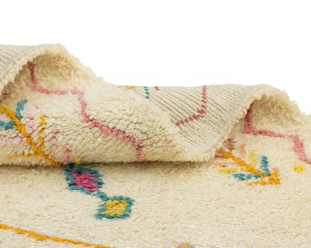 Close-up of a hand-knotted wool rug with a white base, featuring abstract, colorful designs in blue, yellow, and pink.