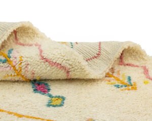 Close-up of a hand-knotted wool rug with a white base, featuring abstract, colorful designs in blue, yellow, and pink.