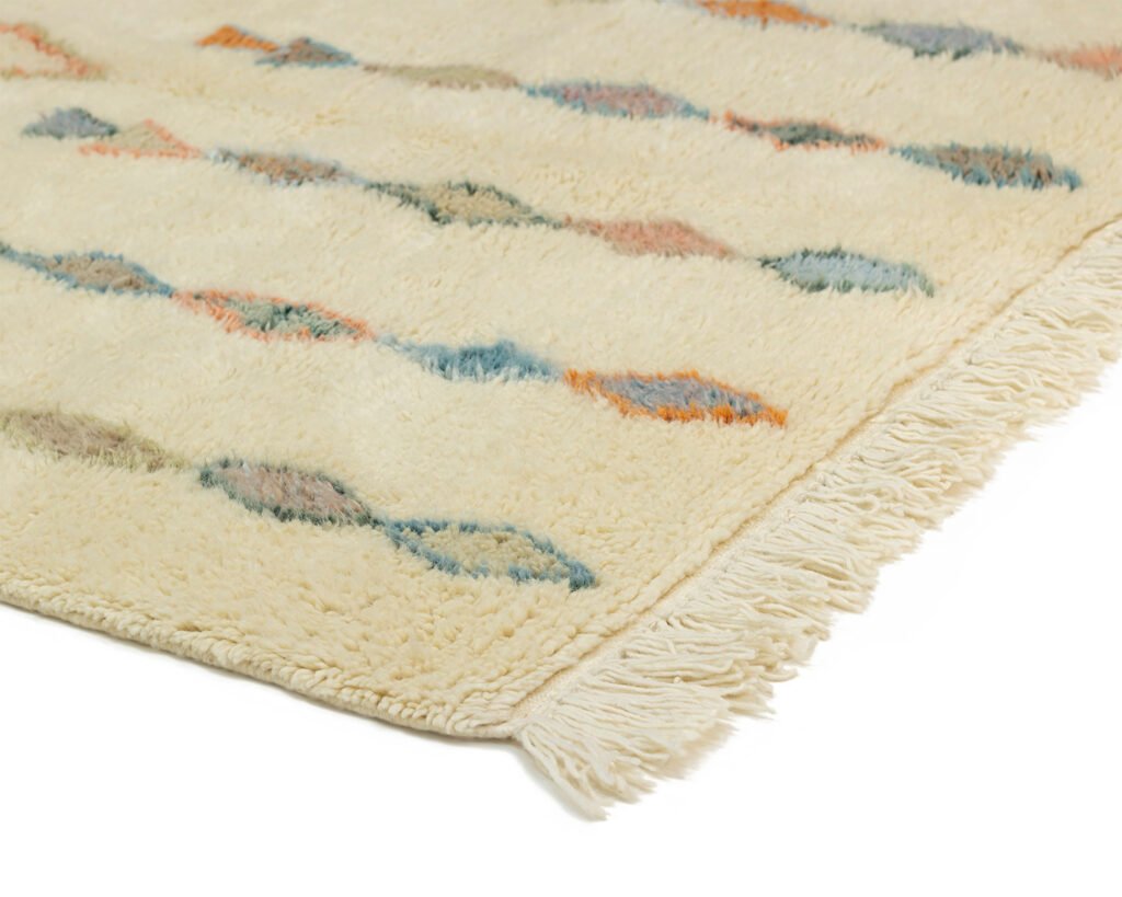 A corner of an artisanal rug with multicolored diamond patterns and fringed edges. This authentic Moroccan piece features hues of blue, orange, and gray, showcasing a beautiful blend of tradition and craftsmanship.
