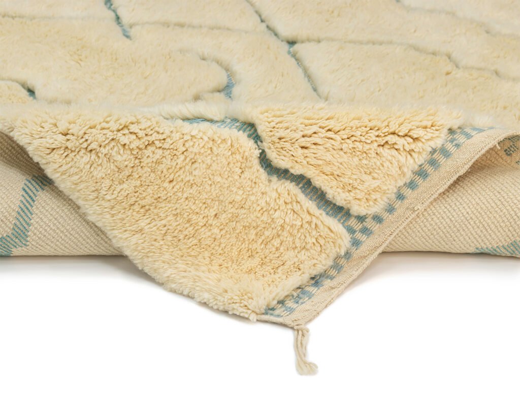 The image showcases a close-up of a cream-colored fluffy Moroccan rug with a geometric pattern, highlighting its soft texture and woven backing.