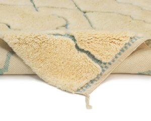The image showcases a close-up of a cream-colored fluffy Moroccan rug with a geometric pattern, highlighting its soft texture and woven backing.