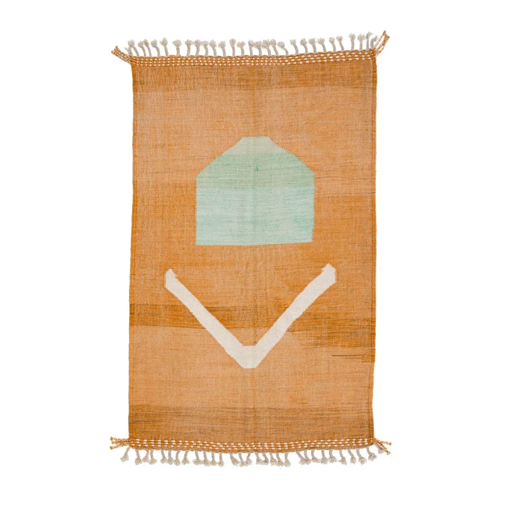 A rectangular flatweave rug with fringed edges, showcasing an orange background, a teal pentagon shape, and a white V-shape design.