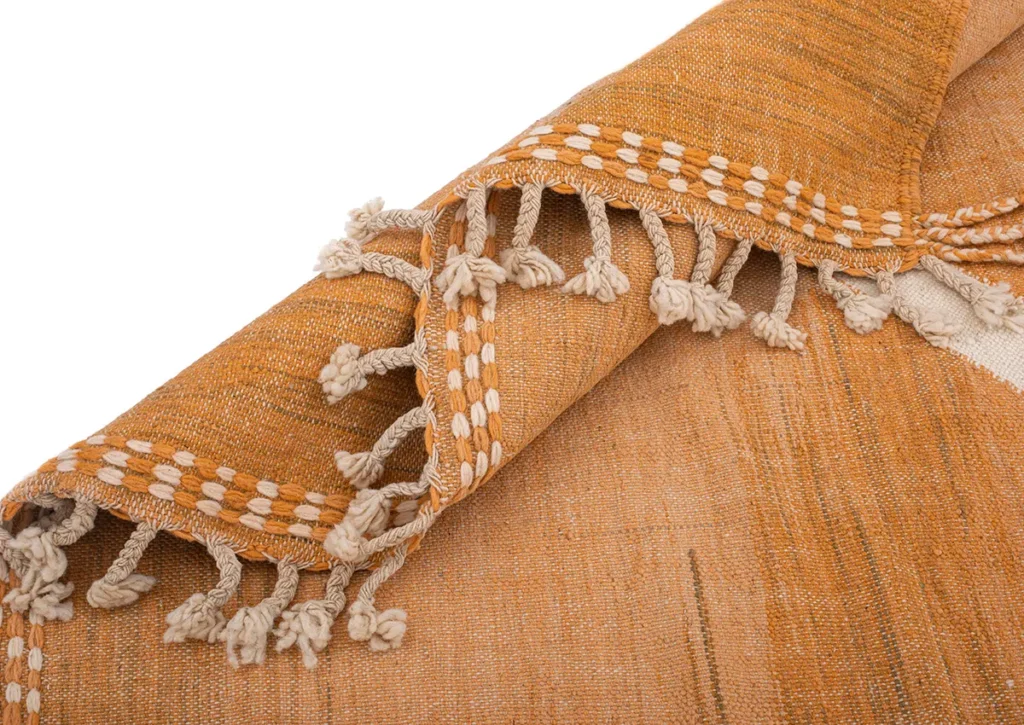 Close-up of a Moroccan rug with orange woven fabric, featuring intricate white embroidery and tassels along the edge.