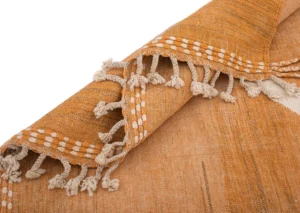 Close-up of a Moroccan rug with orange woven fabric, featuring intricate white embroidery and tassels along the edge.