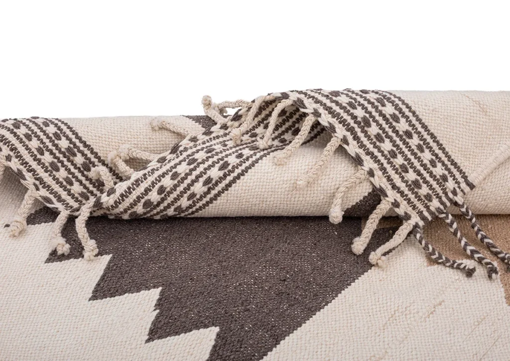 This Moroccan rug features a folded, woven design with a geometric zigzag pattern and tasseled edges in black and white.
