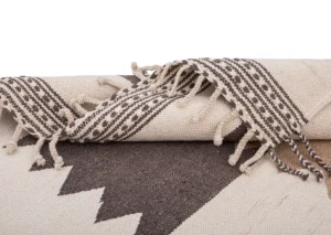 This Moroccan rug features a folded, woven design with a geometric zigzag pattern and tasseled edges in black and white.